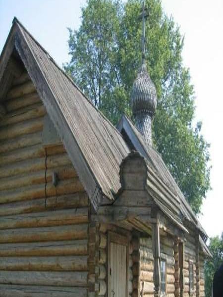 Деревянная церковь с куполом и крестом на фоне зеленых деревьев