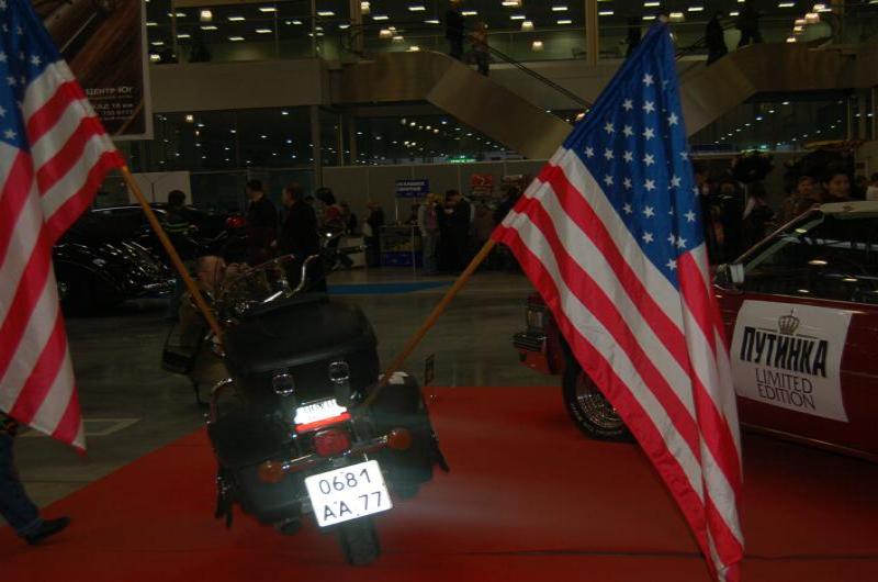 Мотоцикл на красной дорожке с двумя американским флагами и красным автомобилем