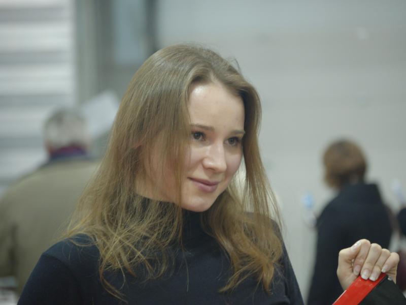 Молодая женщина с длинными светло-каштановыми волосами в черном тurtleneck