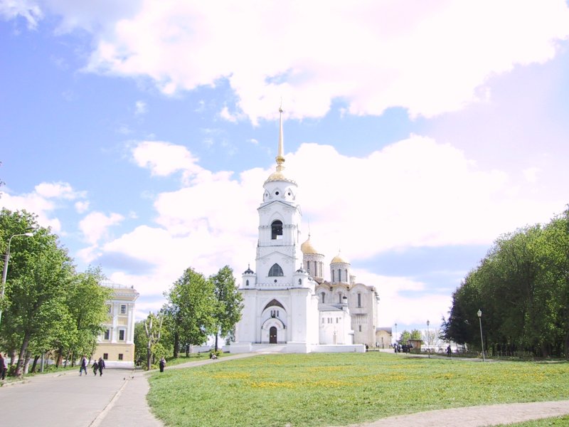 Белокаменная церковь с золотым куполом и шпилем на фоне голубого неба