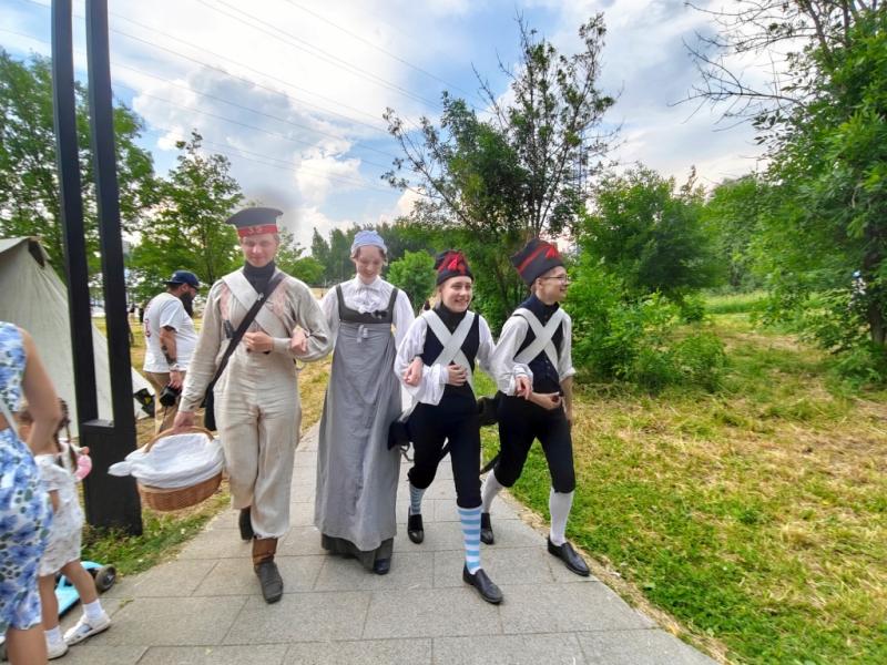 Times And Epochs 2026: группа в исторических костюмах на аллее между деревьями и палатками